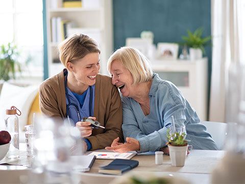 Caregiver laughing with senior female patient while checking her glucose levels.