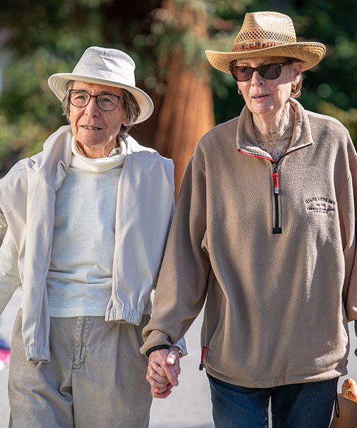 Two older women walking hand-in-hand after buying groceries.