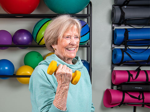 Senior woman lifting yellow weights in an exercise room.